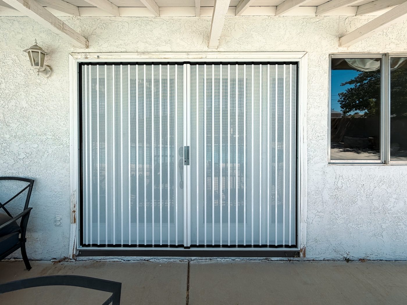 White folding screen closed across a pair of patio doors under a pergola