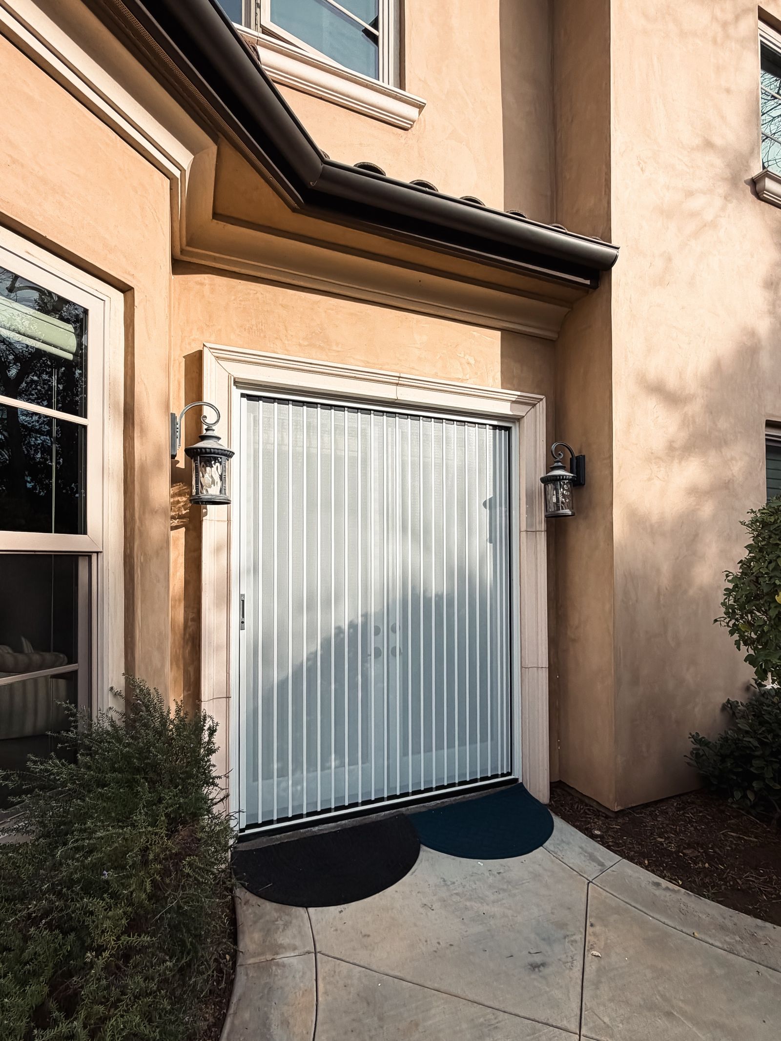 A white TuffFold folding screen closed across stucco French doors in afternoon light