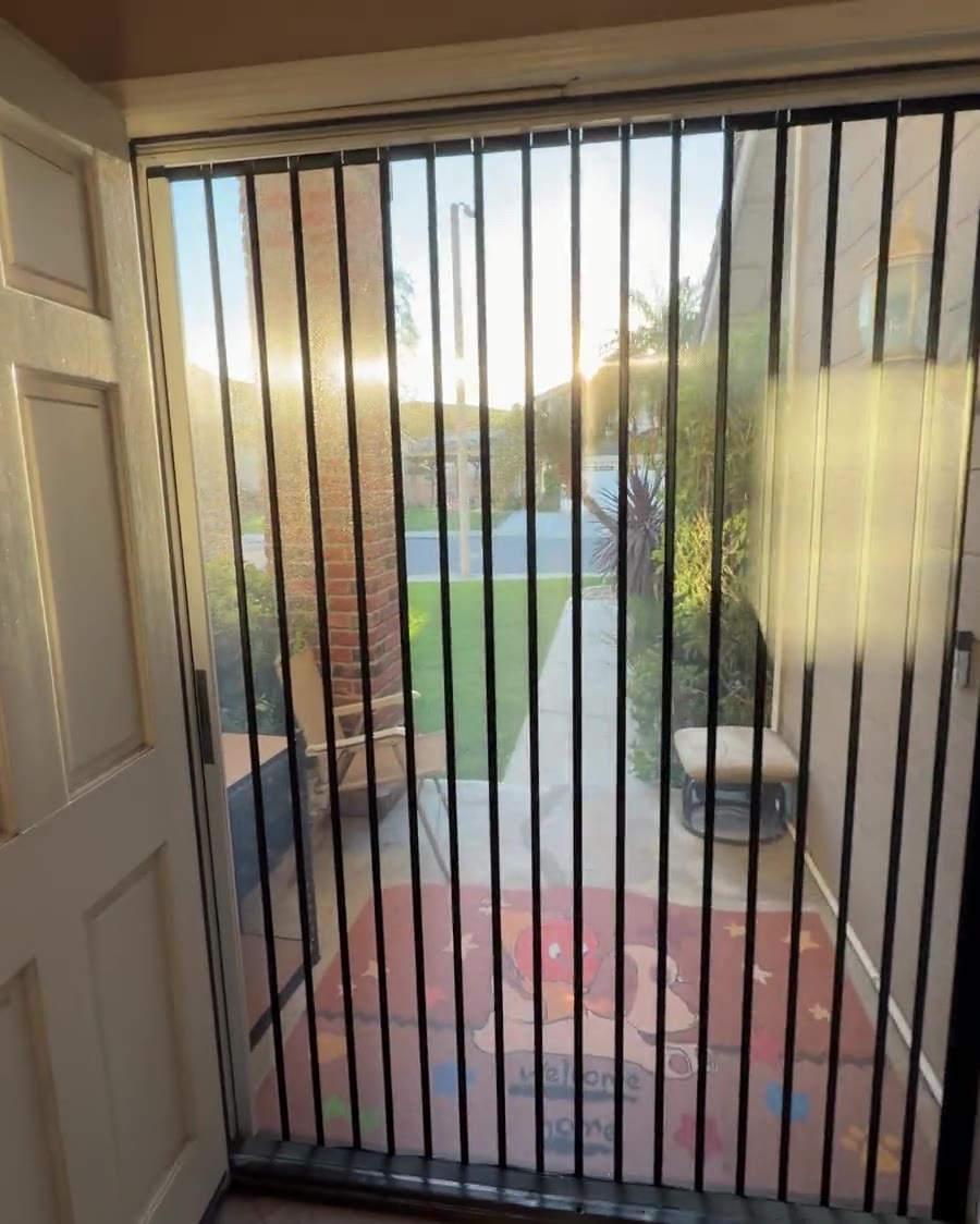 View from inside a home through a closed black TuffFold screen to a sunny yard